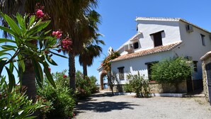 A white building with a tiled roof, surrounded by greenery and palm trees. - Finca Ortiz with private pool for 6 people and fantastic views (Cómpeta)
