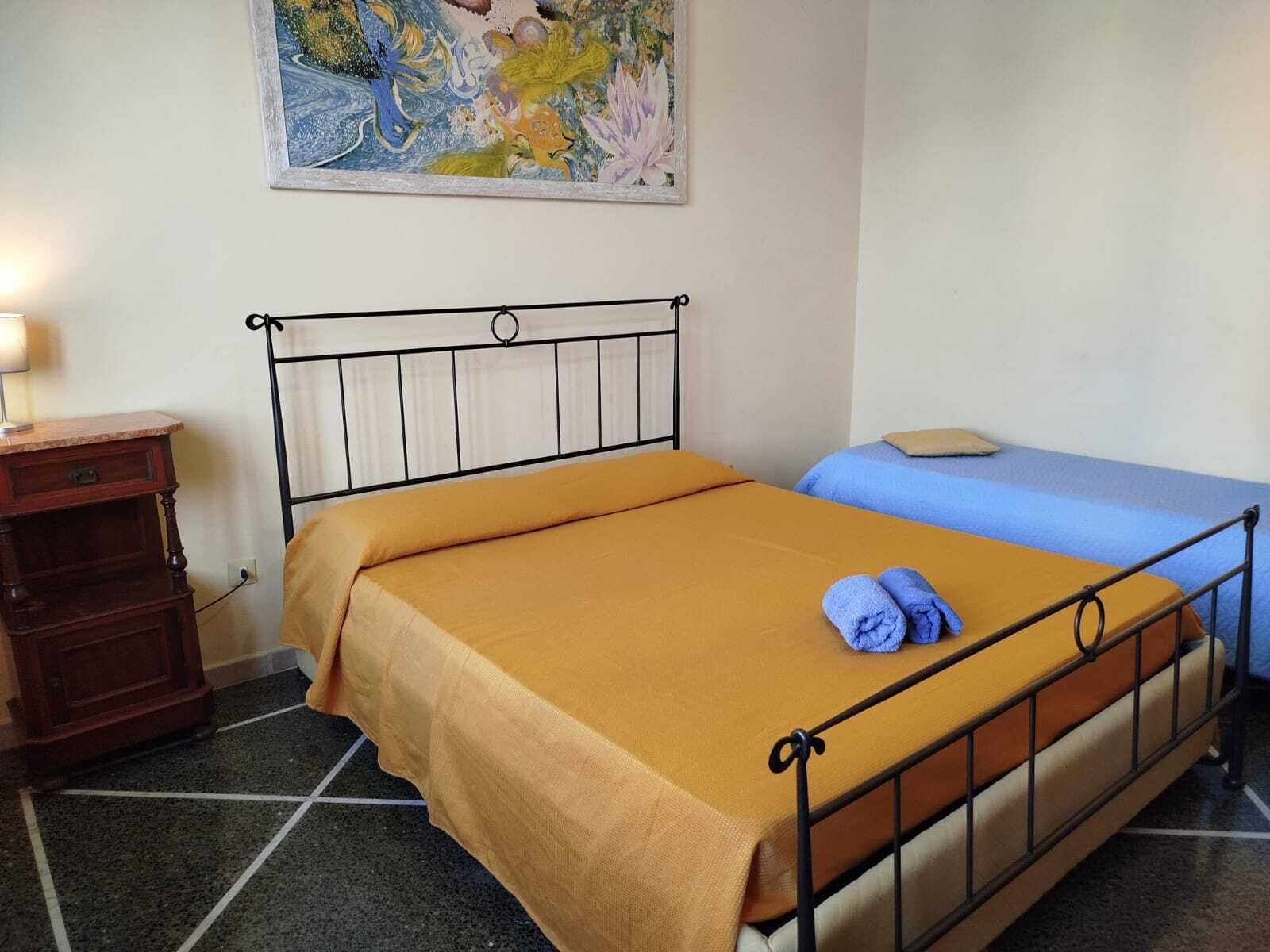 Una cama individual con estructura metálica, una mesita de noche de madera y un cuadro en la pared.