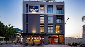 A modern hotel with a prominent sign, outdoor seating, and a view of the street. - City Life Demir Hotel (Fethiye)