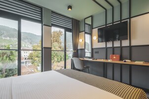 Habitación de hotel con una cama grande, un escritorio con silla, televisión y vistas al exterior.