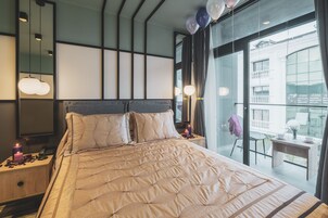 Una habitación de hotel moderna con una cama grande, una mesita de noche con teléfono y velas, un espejo y vistas a la ciudad a través de amplios ventanales.