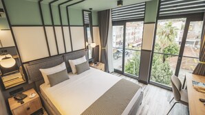 A modern hotel room with a large bed, a desk, and a view of the city through large windows. - City Life Demir Hotel (Fethiye)