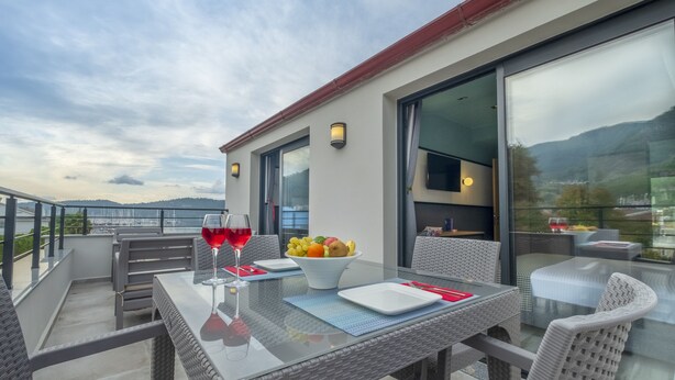 A balcony with wicker furniture, a glass table, and a bowl of fruit. - City Life Demir Hotel (Fethiye)