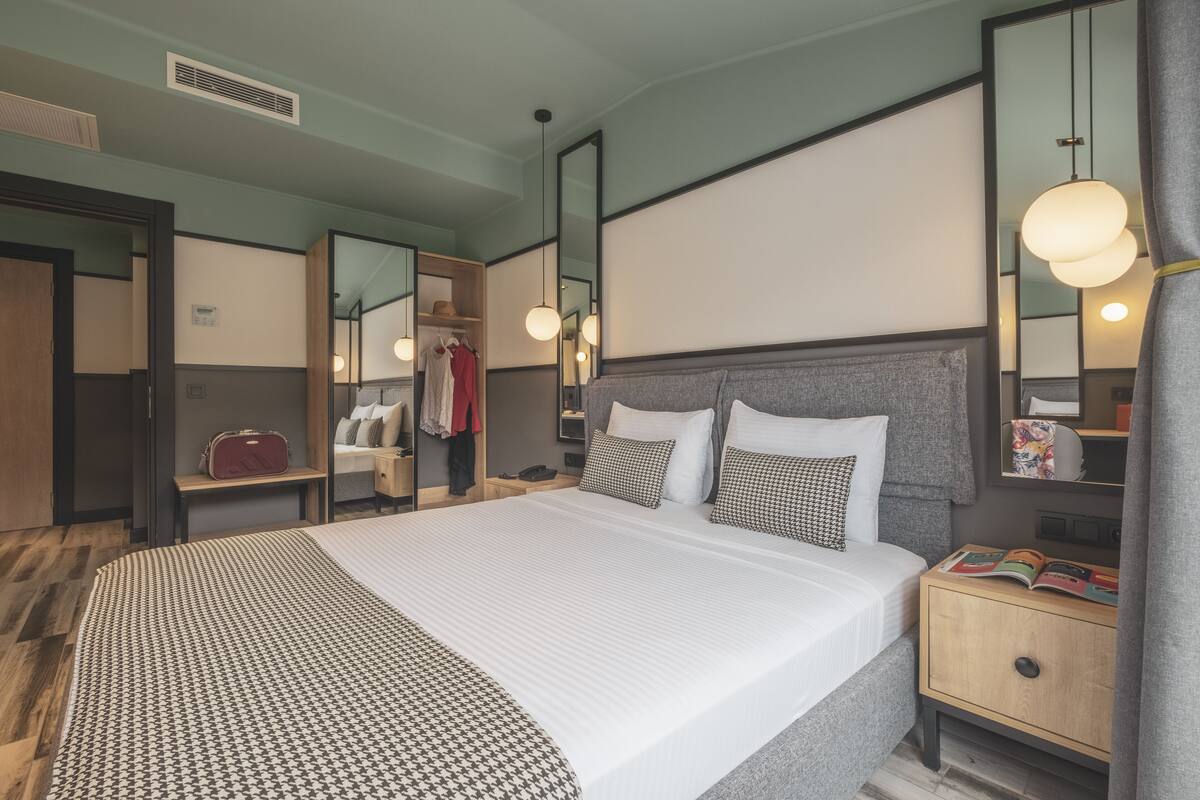 A hotel room with a large bed, bedside tables, a wardrobe, and a mirror.