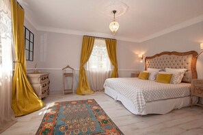 A bedroom with a large bed, a chandelier, a patterned rug, and a window with curtains. - Charm, luxury, stunning views, spacious villa with heated pool, aircon and games (Le Bar-sur-Loup)