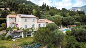 Una villa de piedra con techo de tejas, rodeada de exuberante vegetación y una piscina.