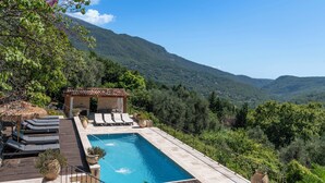 Une piscine sur le toit, dotée de chaises longues, d’une pergola et offrant une vue sur un paysage montagneux.