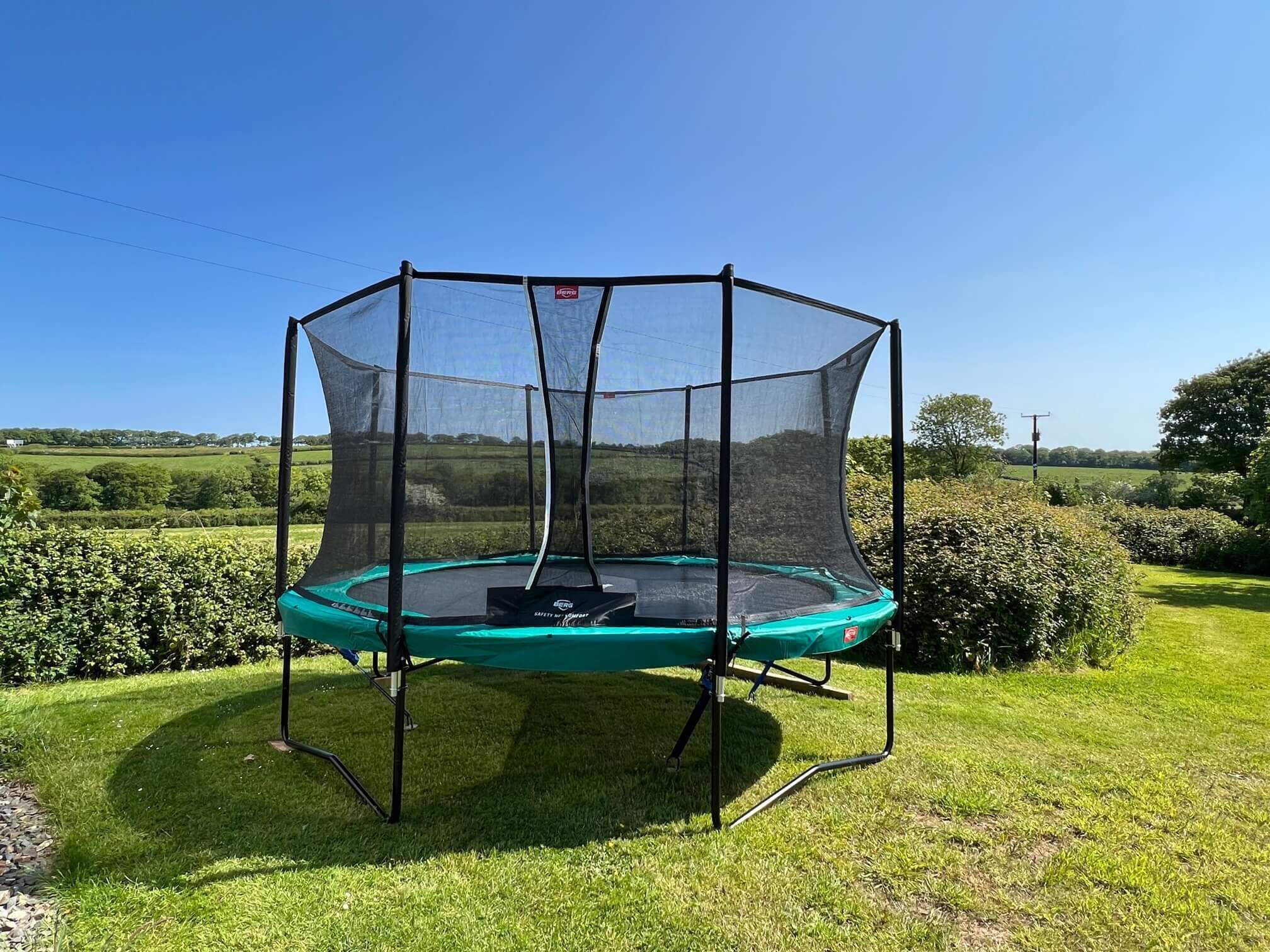 Un trampoline doté d’un filet de protection, installé dans un espace extérieur recouvert d’herbe.