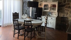 Un coin repas comprenant une table ronde, des chaises, un buffet blanc aux portes vitrées et un mur en pierre.