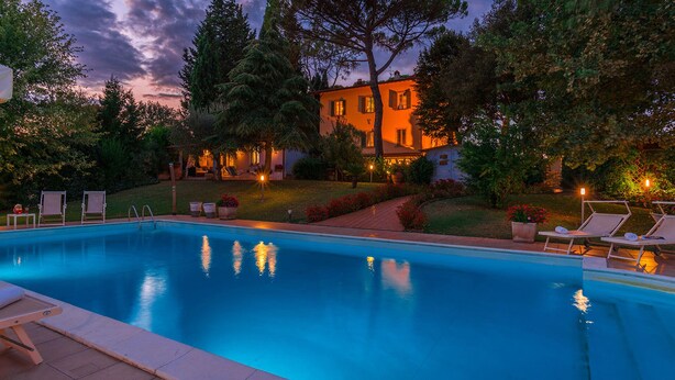 A swimming pool with lounge chairs, surrounded by a garden and a building with a warm glow. - Villa Leonardo 30+6, Emma Villas (Figline e Incisa Valdarno)