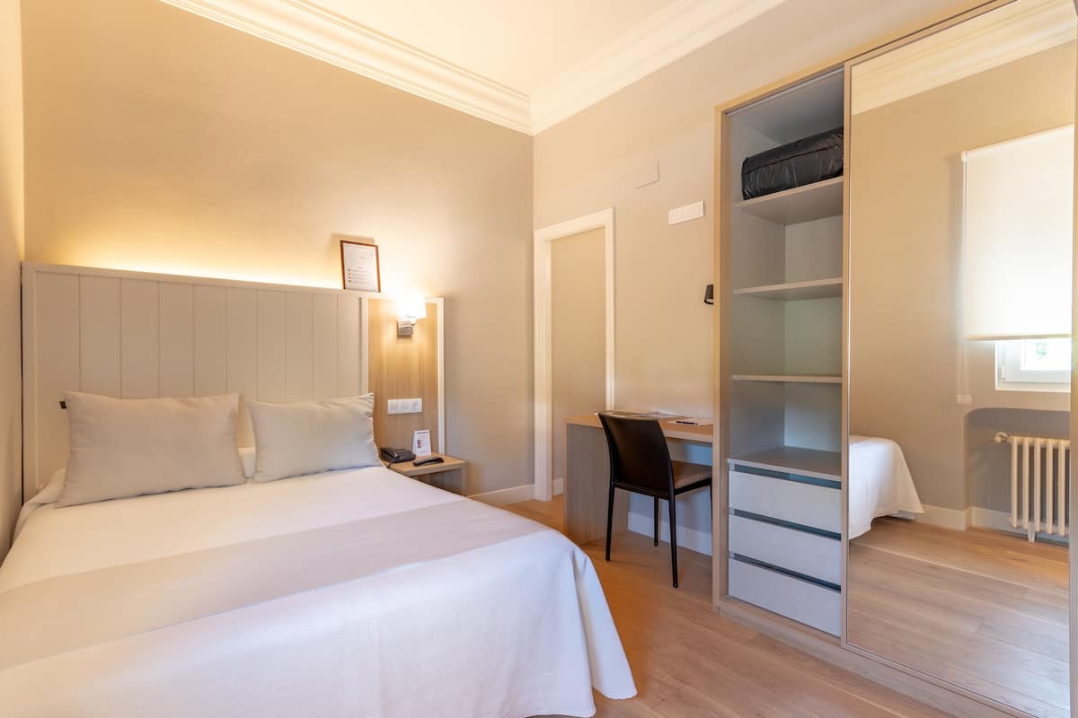 Een slaapkamer met een bed, nachtkastje, bureau, stoel en een inloopkast.