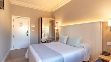 A hotel room with a large bed, bedside table, and a mirror.