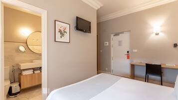 Habitación de hotel con cama, escritorio y silla, televisión, baño con espejo y un cuadro en la pared.