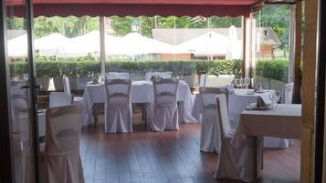 Un área de comedor al aire libre con mesas y sillas, cubierta por un toldo rojo y manteles blancos.