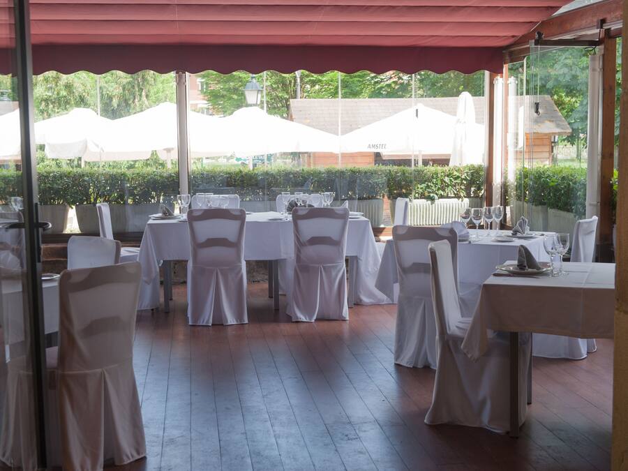 Un área de comedor al aire libre con mesas y sillas, cubierta por un toldo rojo y manteles blancos.