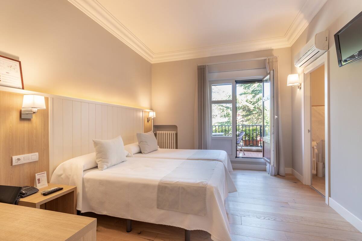 Een hotelkamer met twee bedden, een bureau met telefoon, een radiator en uitzicht op het buitengebied.