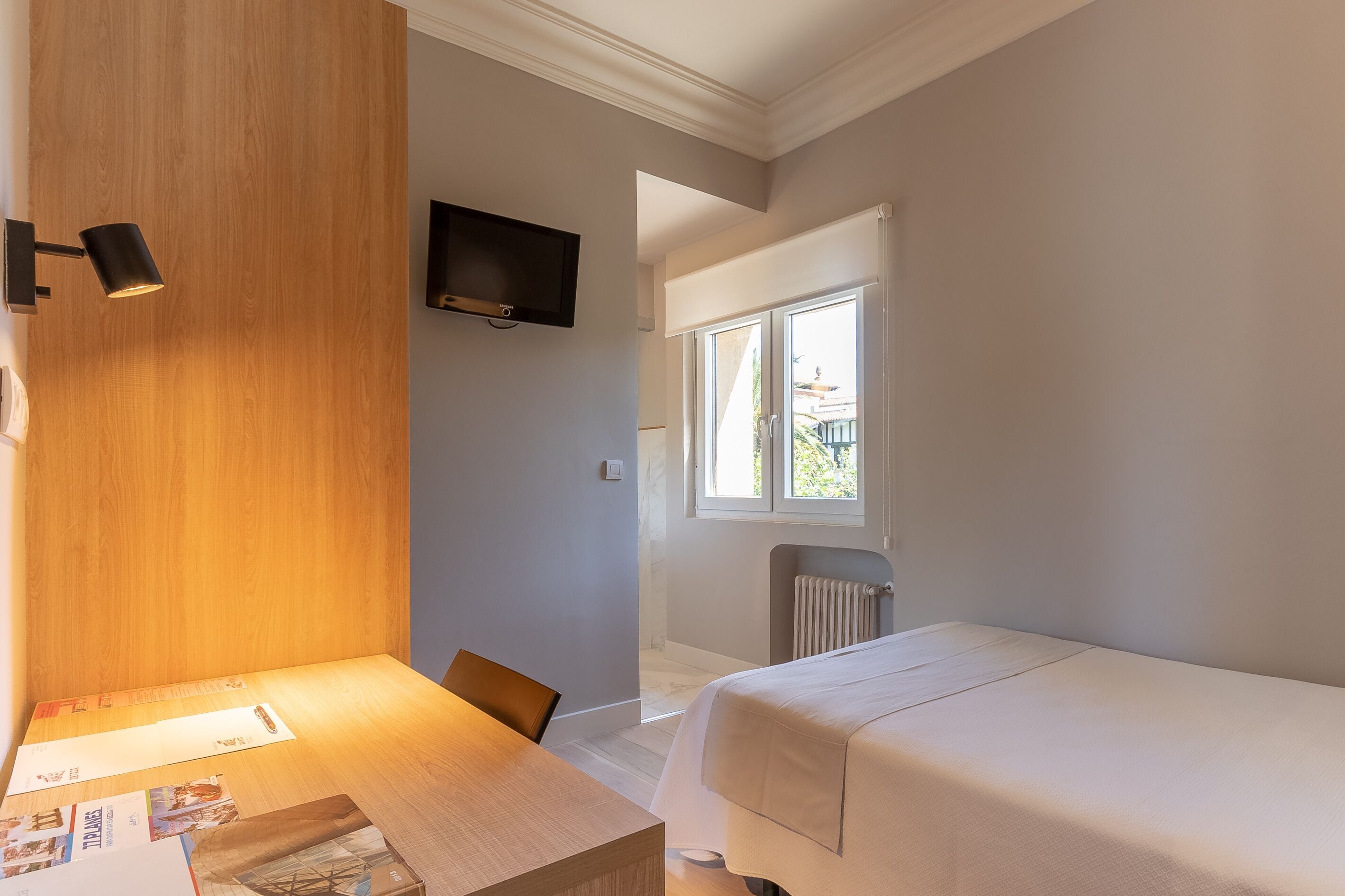 Een slaapkamer met een houten hoofdbord, nachtkastje, bed, tv aan de wand en een raam met uitzicht.