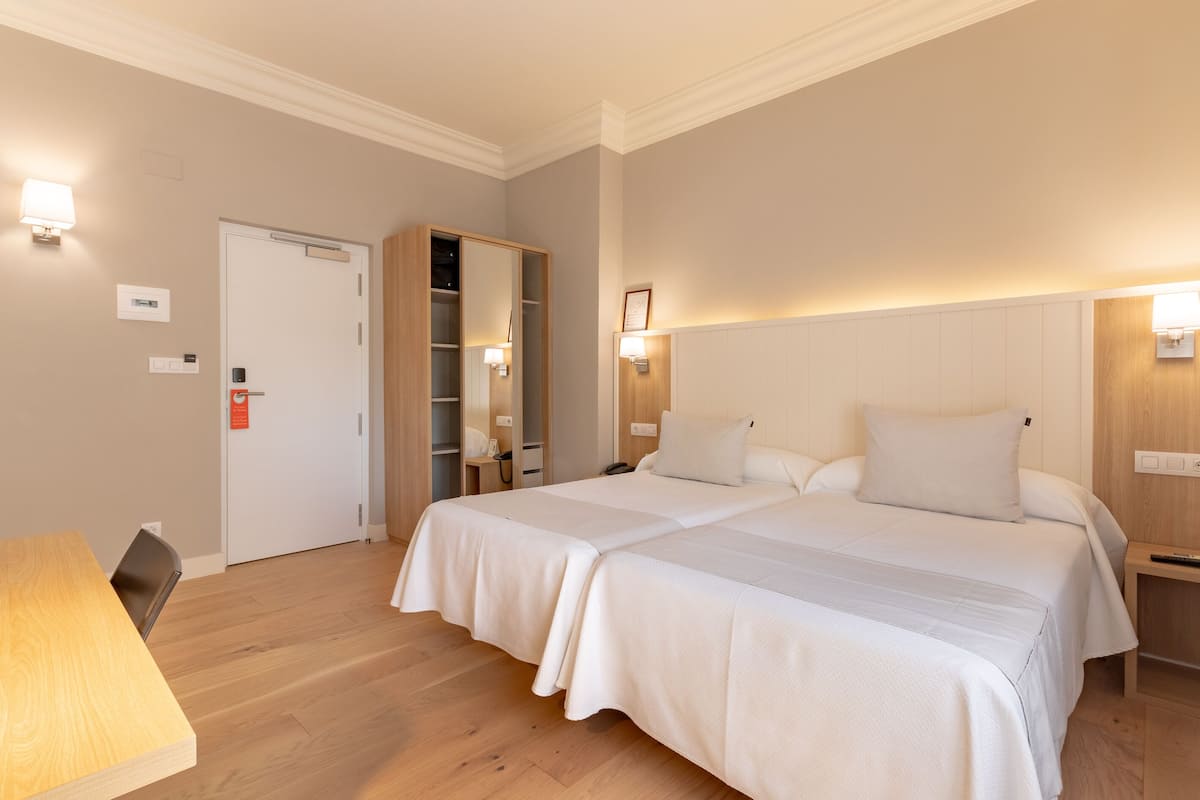 Een hotelkamer met een tweepersoonsbed, een houten bureau, een kledingkast en een nachtkastje met een lamp.