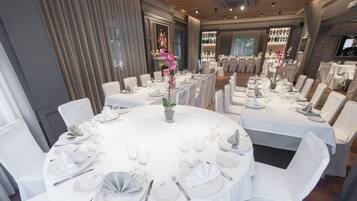 Un comedor formal con mesas redondas dispuestas para varios invitados, con manteles blancos, sillas y elegantes centros de mesa.