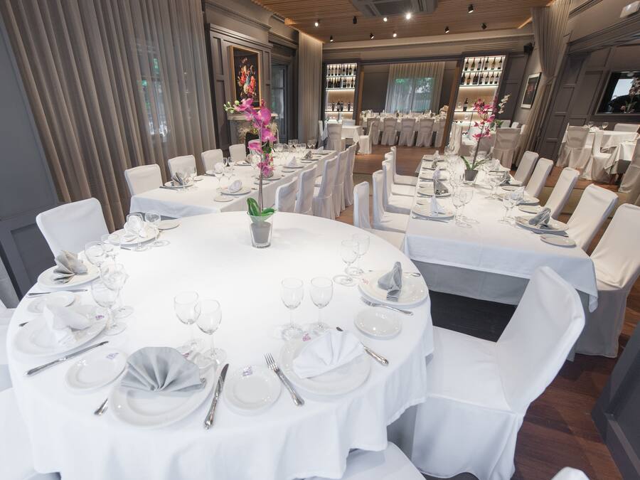 Un comedor formal con mesas redondas dispuestas para varios invitados, con manteles blancos, sillas y elegantes centros de mesa.