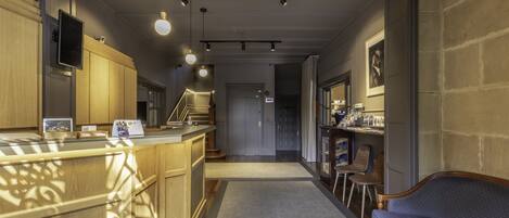 A hotel lobby with a reception desk, wooden cabinets, a blue sofa, and a staircase leading to another floor.