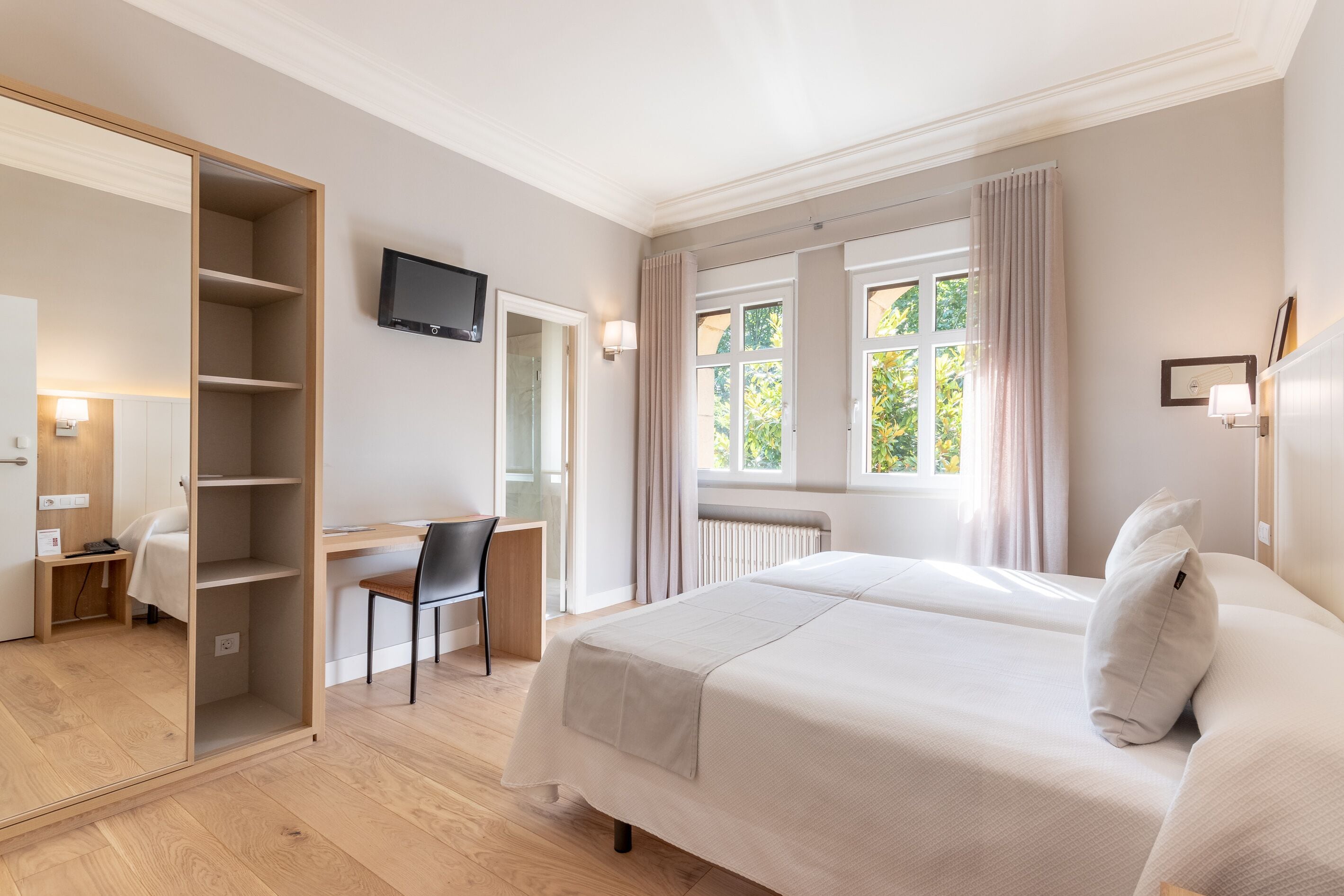 Una habitación de hotel moderna con una cama grande, un escritorio con silla, una televisión y una ventana con cortinas.