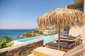 Un espace piscine doté de chaises longues et d’un parasol en chaume, avec vue sur la mer.