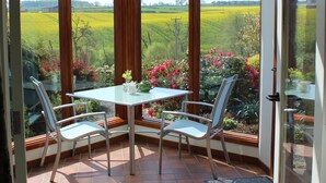 A corner room with a glass table and chairs, a view of a field, and a door leading outside.
