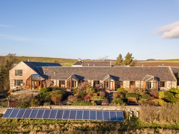 Una hilera de casas de piedra con paneles solares en la fachada, rodeadas de vegetación.