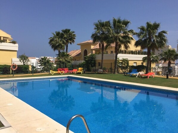 Une piscine avec des chaises longues et des palmiers.