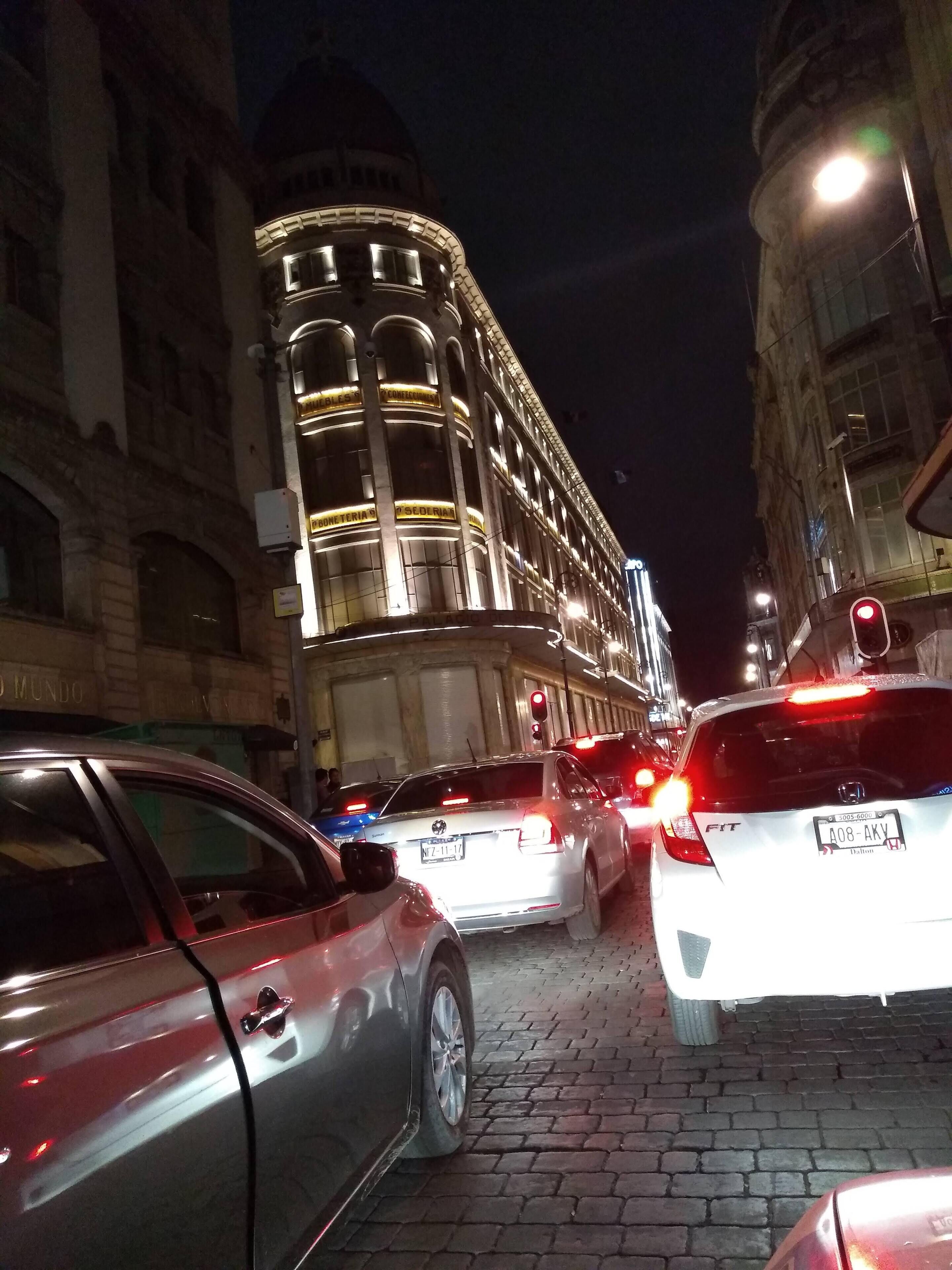 Una calle nocturna con un edificio histórico que cuenta con ventanas de arco y señalización iluminada.