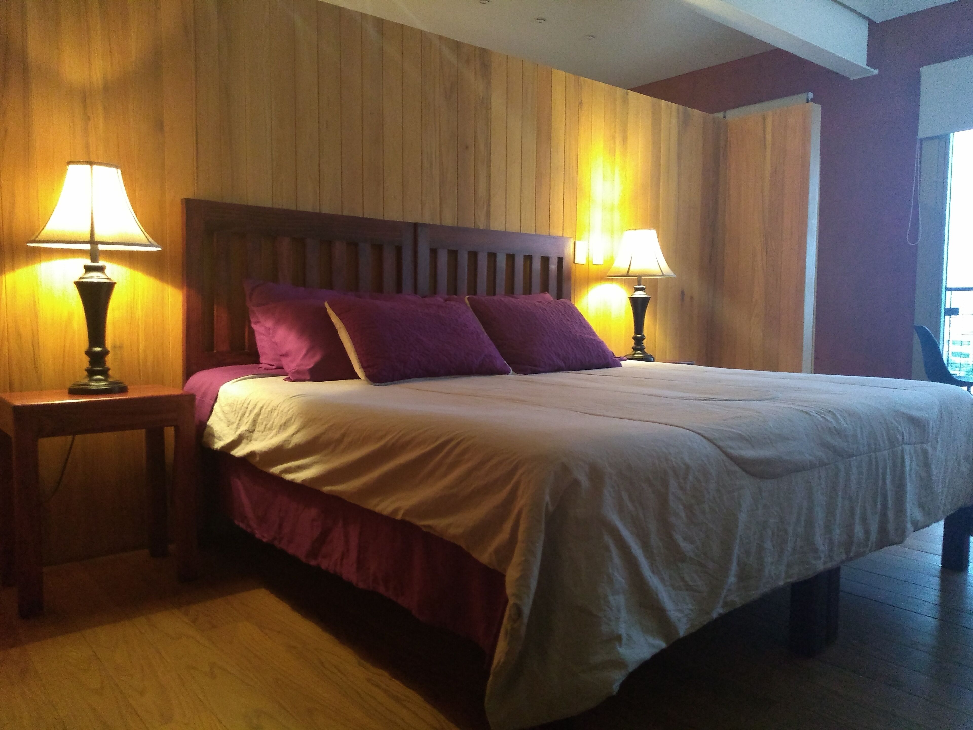 A bedroom with a wooden headboard, two bedside lamps, and a bed with a white and maroon bedspread.