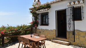 A patio with a wooden table and chairs, a stone wall, and a white building with a tiled roof and a black gate. - Finca Durillo with private pool for 6 people (Competa)