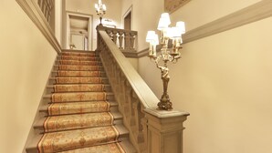 A grand staircase with ornate carpeted steps and a candelabra with multiple lights. - Villa Franchetti - Luxurious Florentine Villa with Swimming Pool (Firenze)