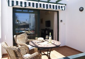A sunlit patio with wicker furniture, a table with a bottle and glasses, and a sliding glass door leading to an interior space. - Modern, spacious apartment with Wifi, Air Con and U.K. TV in Puerto Del Carmen (Puerto del Carmen)