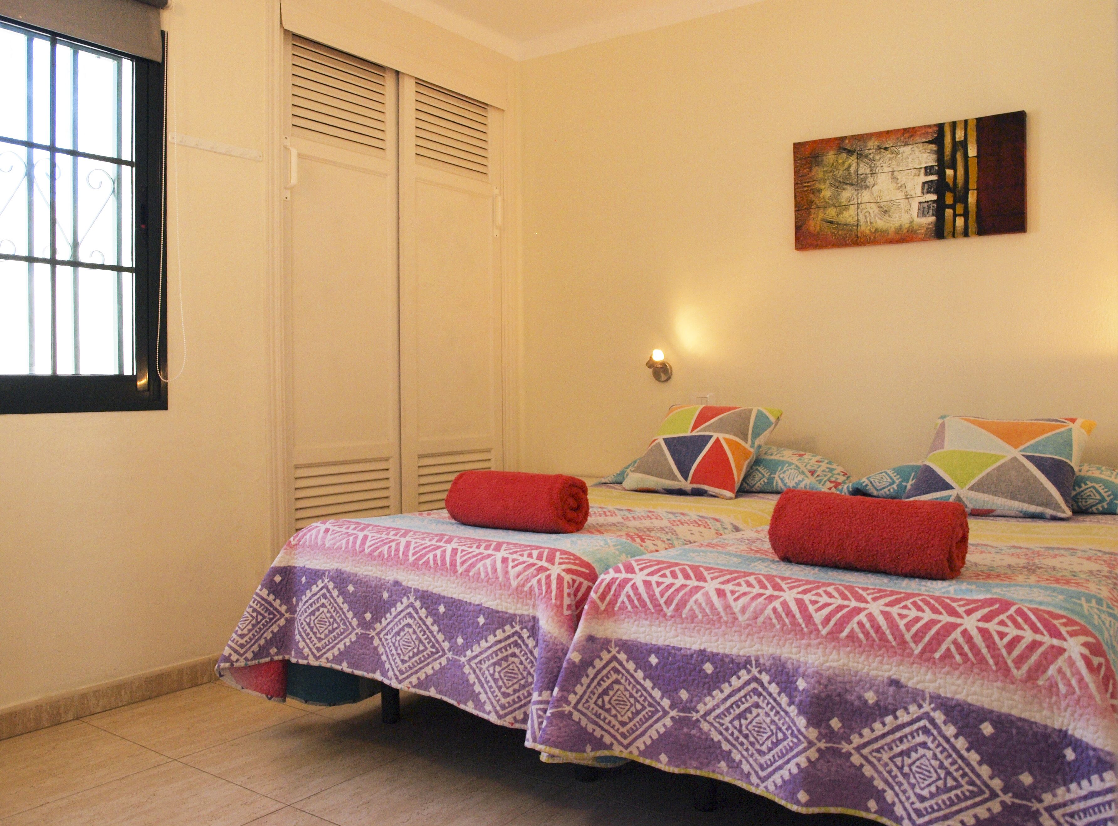 A bedroom with a bed, a window, a wall-mounted artwork, and a light fixture.