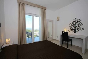 A hotel room with a large bed, a desk with a chair, a decorative tree, and a balcony with a table and chairs. - Rea C504. Pool, massages, restaurant, cocktail bar. For families, beach at 7km. (Ostuni)