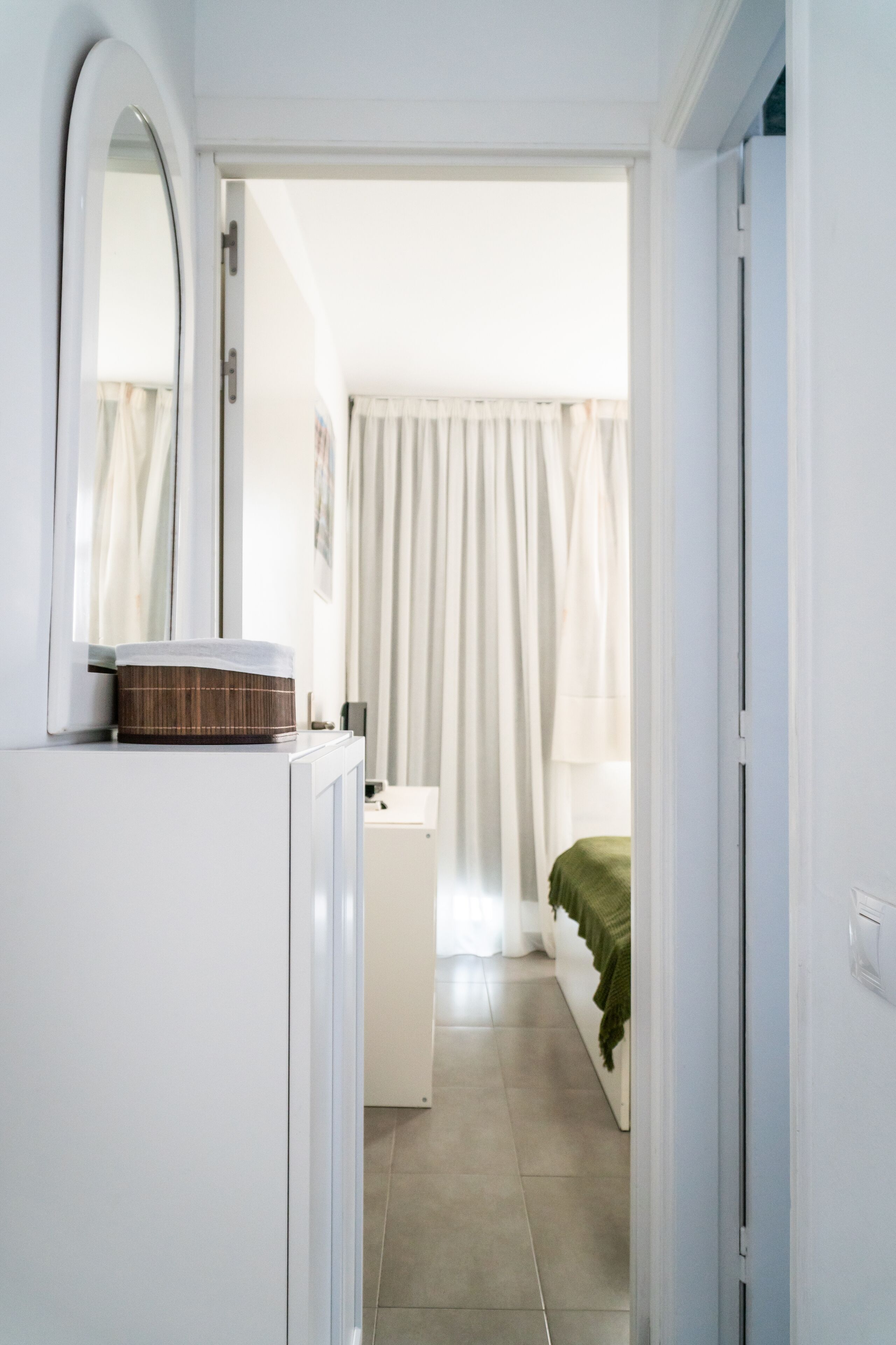 A narrow hallway leading to a bedroom with a bed, a bedside table, and a mirror.