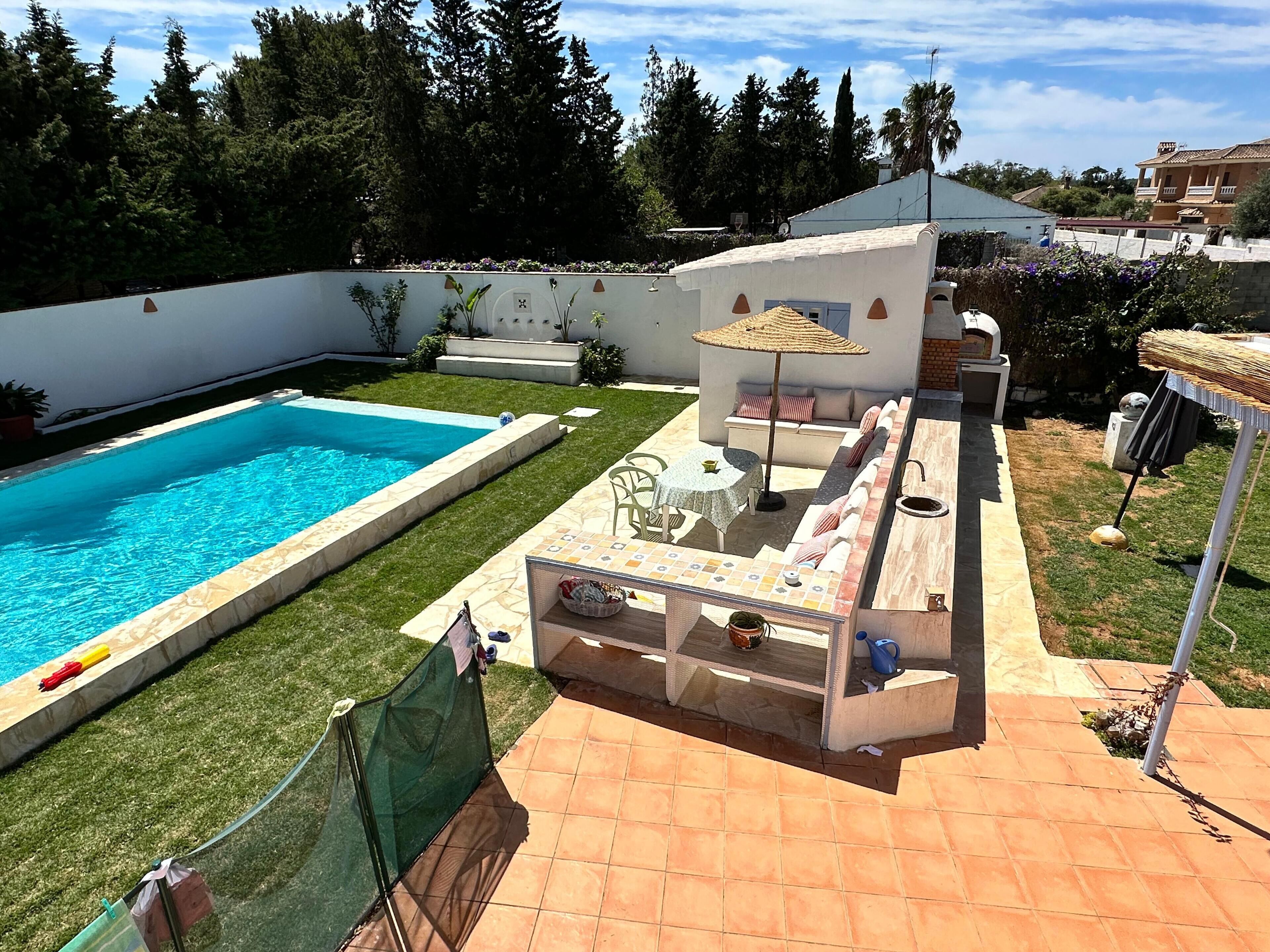 Un patio trasero con piscina, zona de barbacoa y espacio de estar con mesa y sillas.