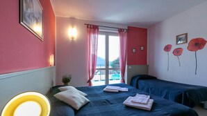 A hotel room with two beds, a large window with curtains, a small balcony, and a wall with poppy decorations.