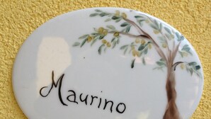 A round, white ceramic plate with a floral design and the name "Maurino" in cursive.