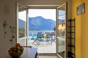 Une chambre avec vue sur les montagnes et une piscine. On y trouve une table avec un saladier rempli de fruits et une chaise.