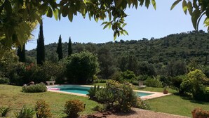 A pool surrounded by a garden with various plants and a view of a hilly landscape. - Charming country house in Silves. (Silves)