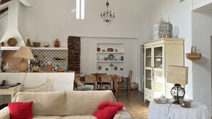 A spacious living room with a high ceiling, a chandelier, a dining area with wooden furniture, and a kitchen with white cabinets. - Charming country house in Silves. (Silves)