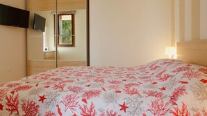 Une chambre à coucher avec un lit, un téléviseur fixé au mur et une fenêtre donnant sur un paysage verdoyant.