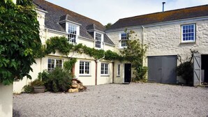A courtyard with a gravel ground, a stone wall, and a building with a stone facade and multiple windows. - Stunning coastal annex with spectacular sea views (Perranuthnoe)