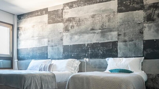 Habitación de hotel con dos camas, un ventanal grande y una pared con textura.