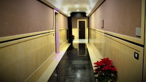 Un pasillo con piso de mármol, una puerta al final y una planta en maceta con flores rojas.