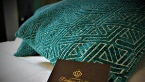 Una cama con un almohadón color turquesa con un estampado y una tarjeta con el logotipo de una corona.