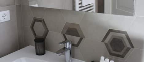 Un baño con un lavamanos blanco, un espejo y un perchero para toallas.